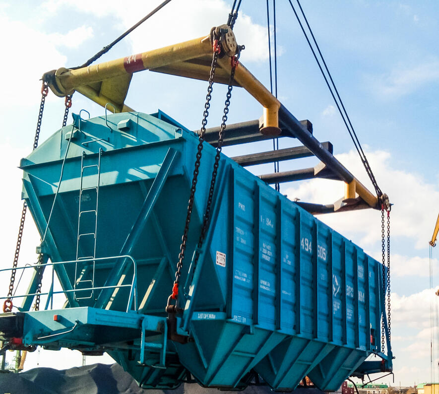 Heavy-duty spreader beam in port operations used for lifting hopper railcars with engineered load distribution.